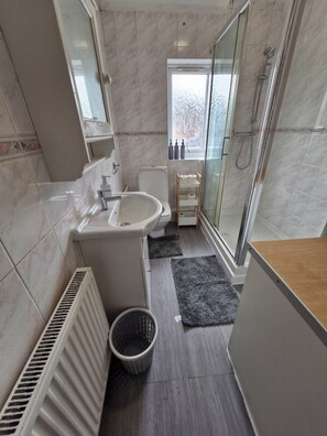 A bathroom with a toilet, sink, shower, and a window with a view.