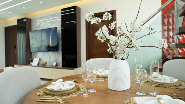 A dining area with a round table set for a meal, a vase with white flowers, and a modern interior design.