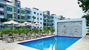 A swimming pool with lounge chairs and umbrellas, surrounded by modern buildings.