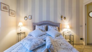 A neatly made bed with floral bedding, two bedside lamps, and a striped wall. - Apartment Saida by Interhome (Castiglioncello)