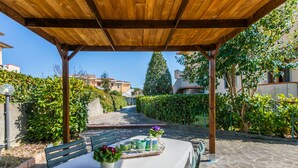 An outdoor patio with a wooden pergola, stone flooring, and a table set for dining. - Apartment Saida by Interhome (Castiglioncello)