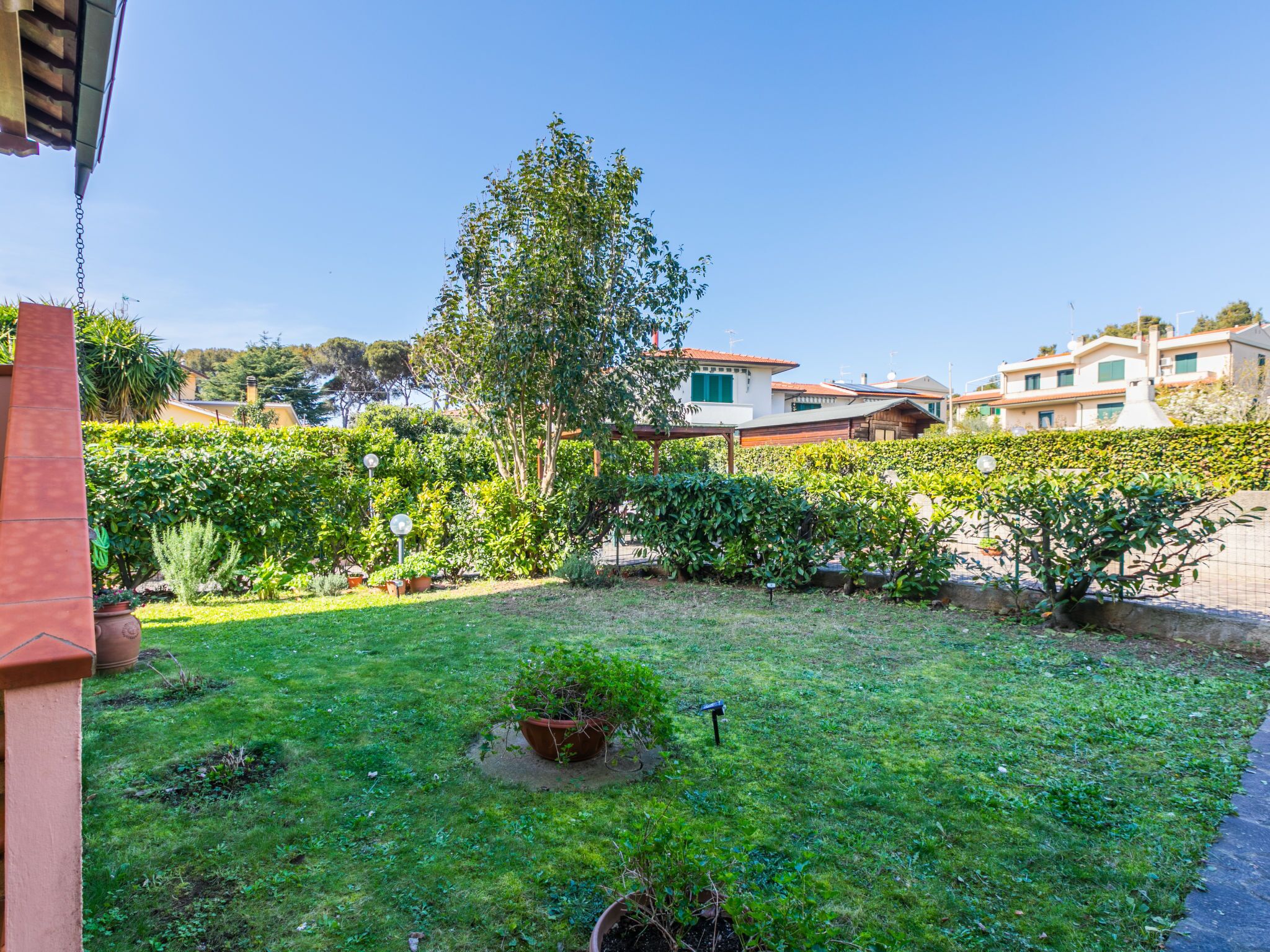 A well-maintained garden with various plants and a lawn, surrounded by buildings with Mediterranean architecture.