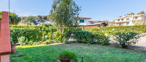 A well-maintained garden with various plants and a lawn, surrounded by buildings with Mediterranean architecture.