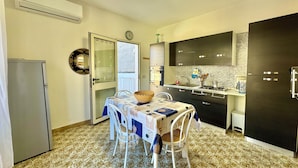 Una cucina compatta con zona pranzo, dotata di frigorifero, tavolo con sedie, forno a microonde e mobili scuri.