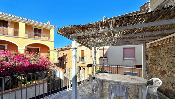 Patio esterno con tavolo e sedie, circondato da muri in pietra e un edificio giallo.