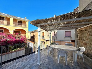 An outdoor patio with a table and chairs, surrounded by stone walls and a yellow building. - "  Happy   Terrace " (Bari Sardo)
