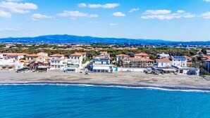 A coastal town with buildings along the beach, a clear sky, and mountains in the background.