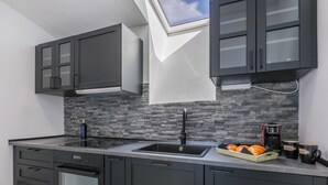 A modern kitchen with dark cabinetry, a stone backsplash, a skylight, and a coffee maker on the counter.