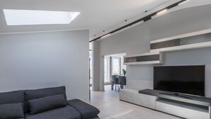 A modern living room with a grey sofa, a glass coffee table, and a flat-screen TV mounted on a wall.