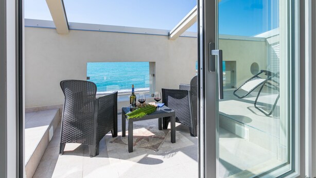 A balcony with a table, chairs, and a bottle of wine.