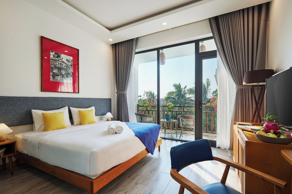 Una camera d'albergo con un letto, una scrivania con una sedia, un balcone con vista e una televisione.