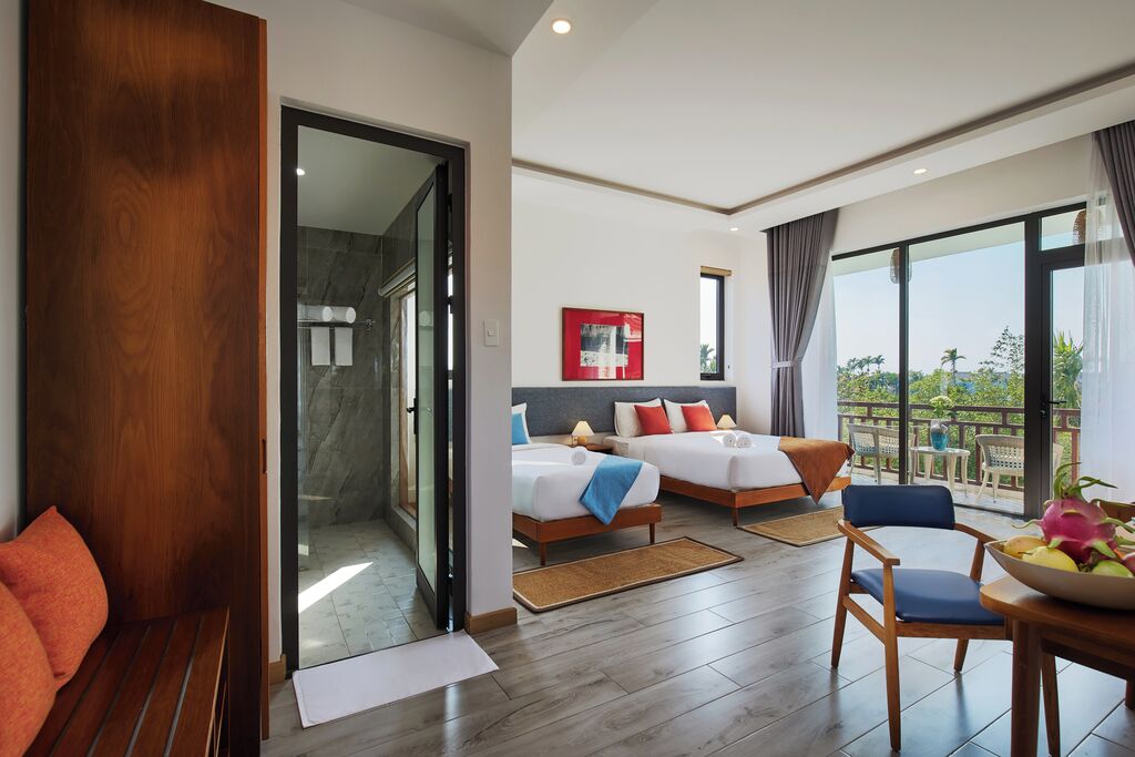 A hotel room with two beds, a balcony, and a dining area.