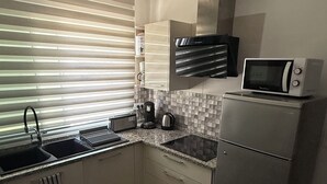A modern kitchen with a stainless steel refrigerator, microwave, and kettle. There is a window with blinds, a sink, and a countertop with a kettle and a coffee maker. - Chic Luxury Appartement In The Heart Of La Marsa _ Walk to the Beach and Cafés (Marsa)
