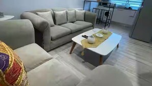 A modern living room with a sofa, a coffee table, and a kitchen area in the background. - Chic Luxury Appartement In The Heart Of La Marsa _ Walk to the Beach and Cafés (Marsa)