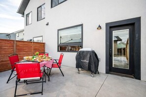An outdoor patio with a table set for a meal, red chairs, and a barbecue grill.