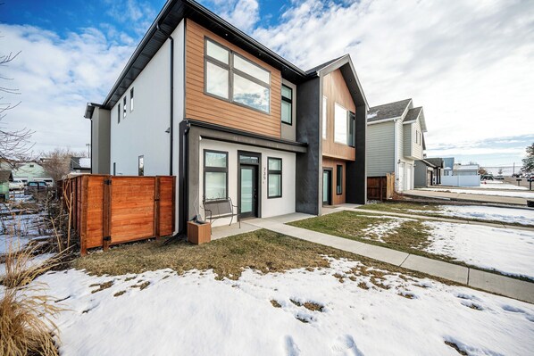 A modern two-story house with a large front porch and a fenced backyard.