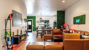 A modern living room with a leather sofa, a dining area with wooden chairs, and a kitchen visible through an open door. - Zen Den — Wellness Retreat, Sauna & Red Light Therapy, Sheridan WY (Sheridan)
