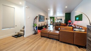 A modern living room with a brown leather sofa, a dining area, and a kitchen visible through an open door. - Zen Den — Wellness Retreat, Sauna & Red Light Therapy, Sheridan WY (Sheridan)