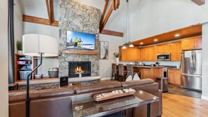 A modern kitchen with wooden cabinets, a stainless steel refrigerator, and a stone fireplace. - Westridge Ski-In/Ski-Out with Private Hot Tub (Breckenridge)