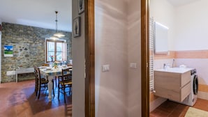 Ein Zimmer mit Steinwand, einem Essbereich mit Tisch und Stühlen sowie einem Badezimmer mit Waschmaschine.