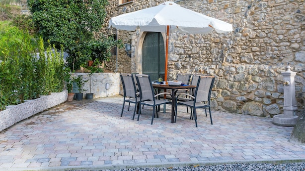 Ein Steinhaus mit einer Terrasse, komplett mit Tisch und Stühlen unter einem weißen Sonnenschirm.