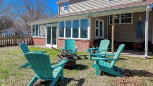 A house with a covered patio, a fire pit, and two green Adirondack chairs.