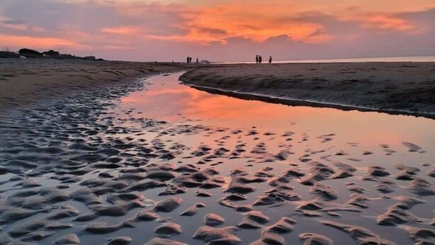 A beach with footprints in the sand and a calm sea.