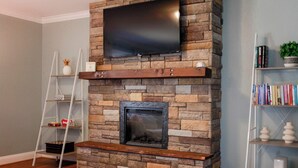 A stone fireplace with a flat-screen TV mounted above it, surrounded by bookshelves and a ladder.