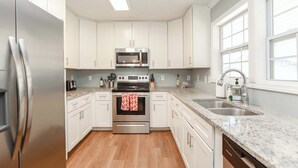 A modern kitchen with white cabinets, stainless steel appliances, a granite countertop, and a window providing natural light.
