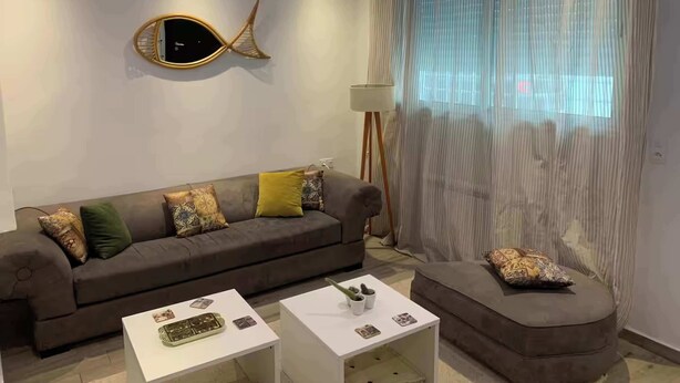 Una sala de estar moderna con un sofá, dos mesas de centro, un adorno en la pared y una lámpara de pie.
