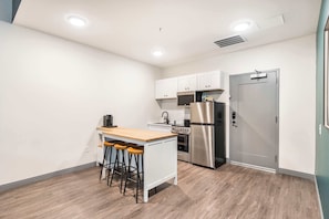 A compact kitchen with white cabinets, a stainless steel refrigerator, a microwave, and a wooden island with stools.