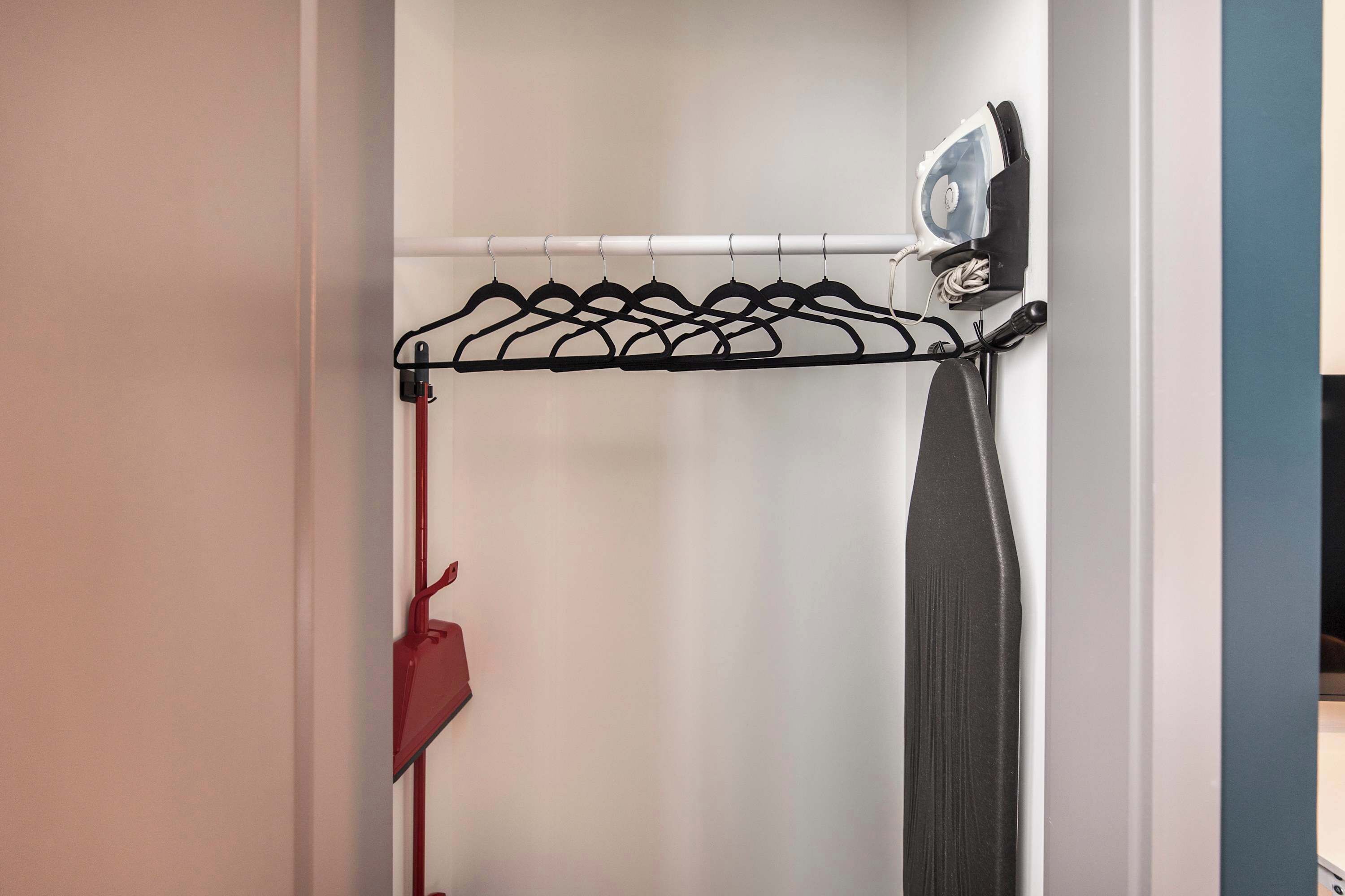 A closet with a black hanger rack, a red hanger, and a steam iron on a white wall.