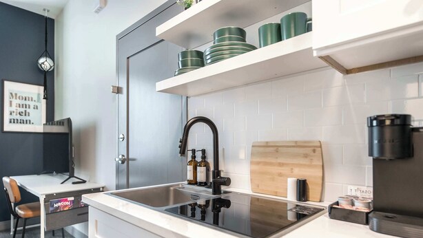 Une cuisine moderne avec un robinet noir, des plans de travail blancs et une planche à découper en bois.