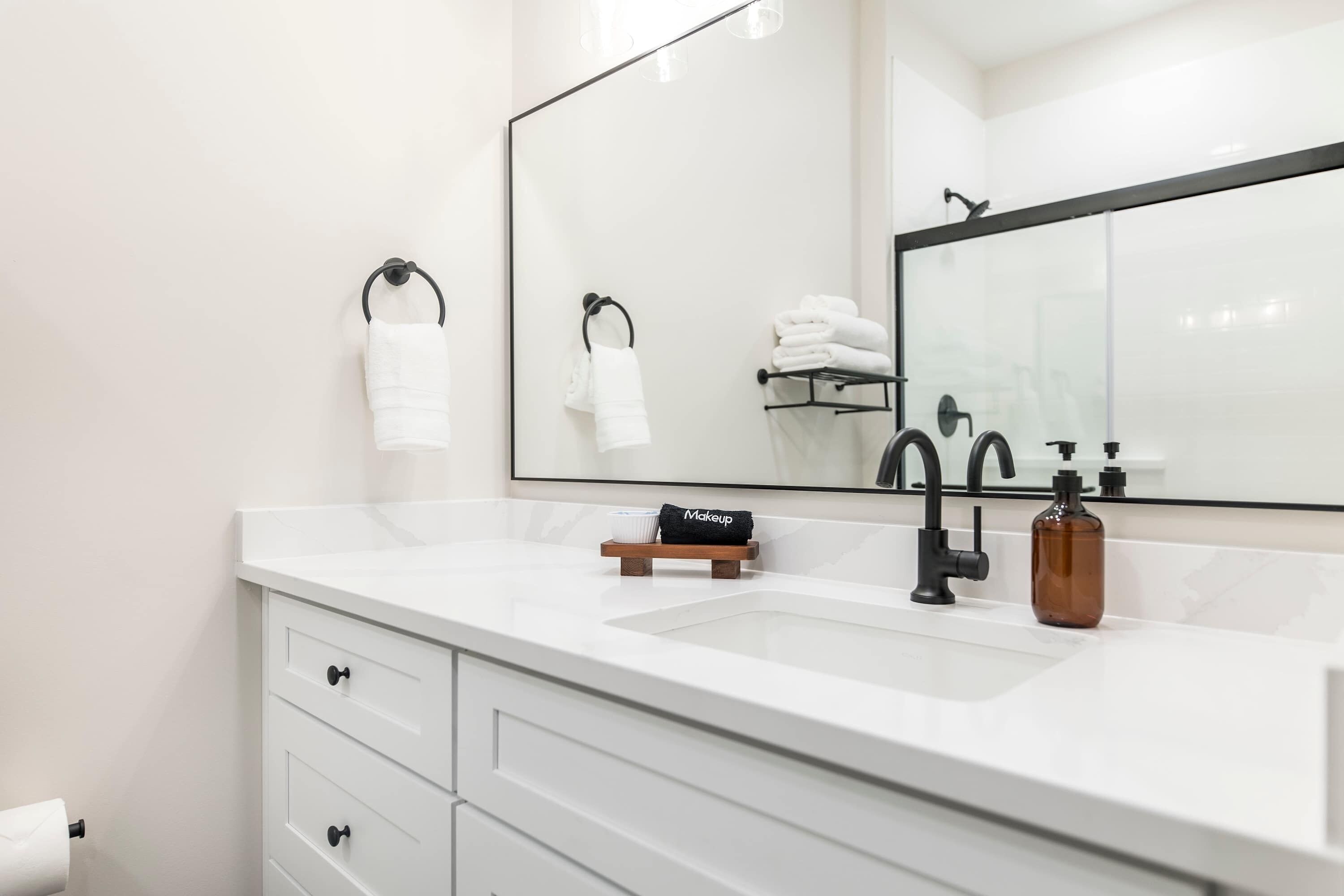 Une salle de bain moderne avec un meuble-lavabo blanc, un grand miroir, un robinet noir et un distributeur de savon.