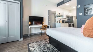 Una habitación de hotel moderna con cama, escritorio, silla, televisor, kitchenette y una alfombra estampada.