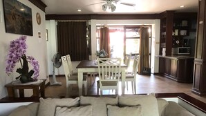 Un salon comprenant un canapé, un ventilateur, une table à manger avec des chaises, et un coin cuisine avec des placards et un four à micro-ondes.