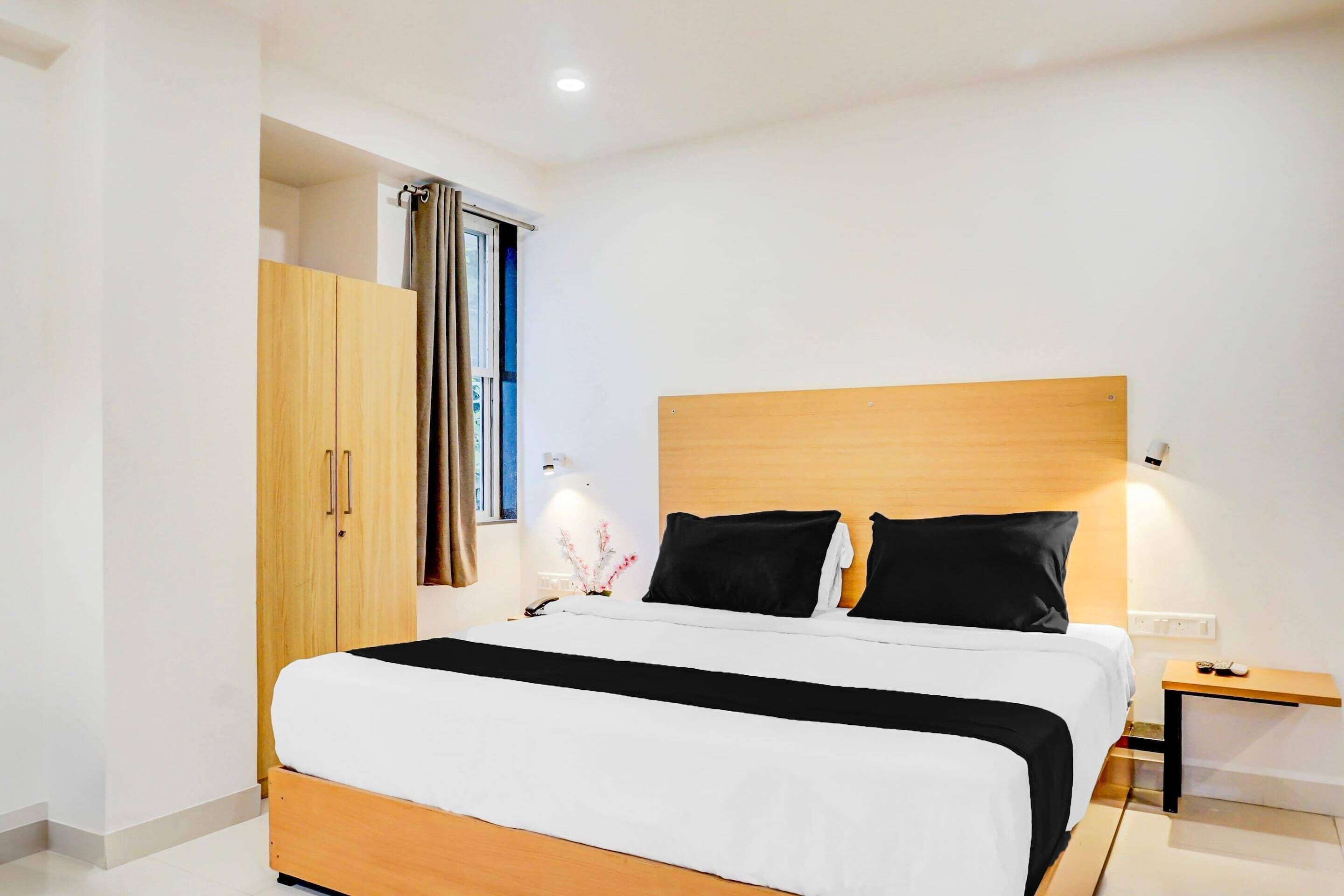 A modern hotel room with a wooden bed frame, a nightstand with a lamp, and a wardrobe.
