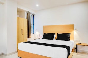 A modern hotel room with a wooden bed frame, a nightstand with a lamp, and a wardrobe. - Elegant Urban Stays at Hadapsar Pune (Pune)