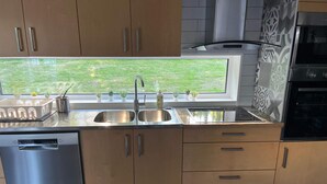 Una cucina con mobili in legno, un lavello in acciaio inox, una lavastoviglie, una finestra con vista sull'esterno e piastrelle decorate.