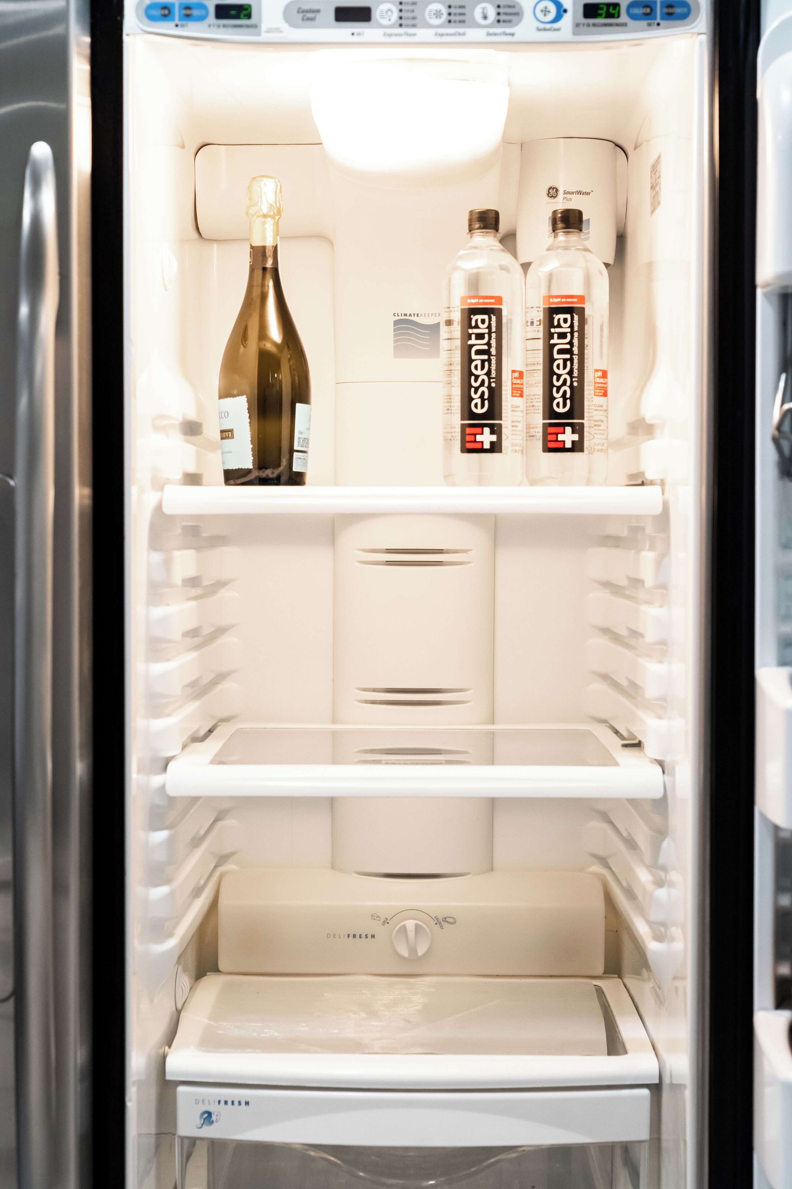 Un refrigerador abierto con una botella de vino y dos botellas de agua Essentia.