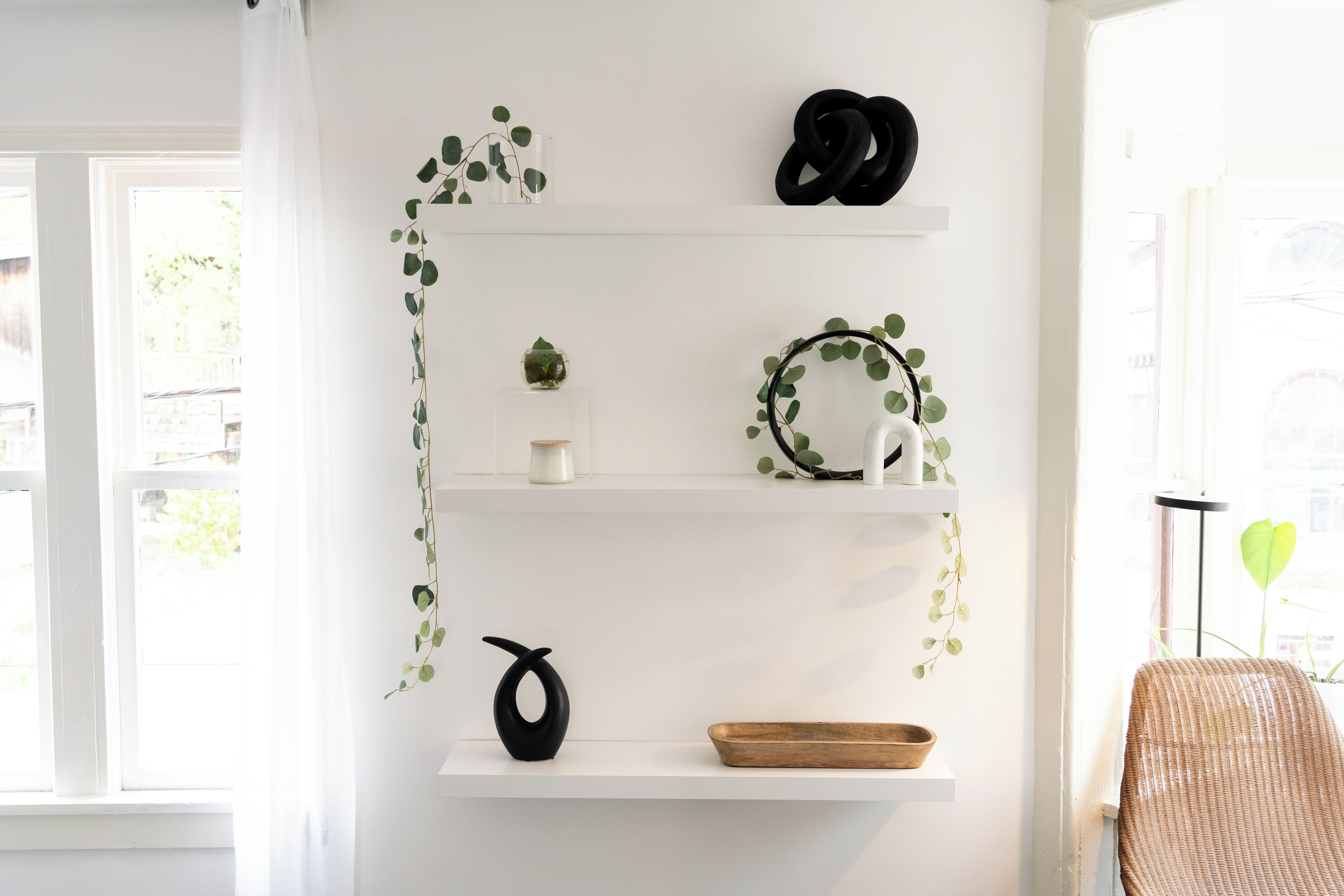 Ein Zimmer mit weißen Wänden, einem Fenster mit Vorhängen und Regalen mit Dekorationen.