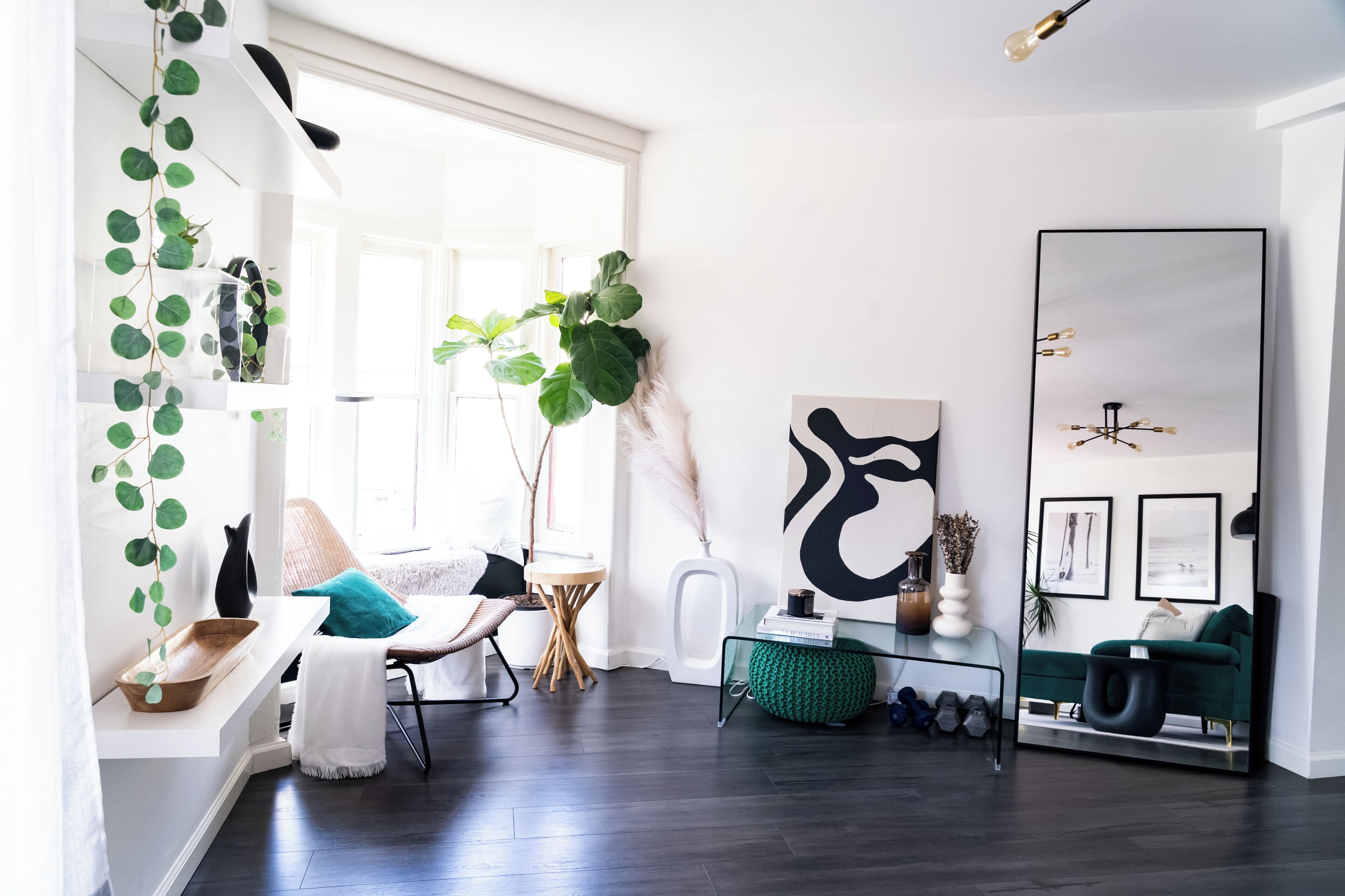 Una sala de estar moderna con un espejo grande, un sofá verde, una mesa de centro y una planta de gran tamaño.