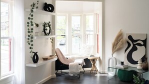 A modern room with a large window, a comfortable chair, a glass coffee table, and a white shelf with decorative items. - The New Hope Loft Walkable & Serene (New Hope)