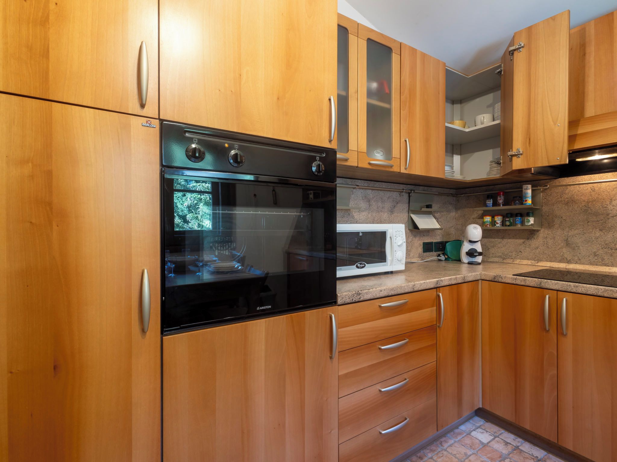 Une cuisine avec des meubles en bois, un four noir, un micro-ondes blanc et un plan de travail en granit.