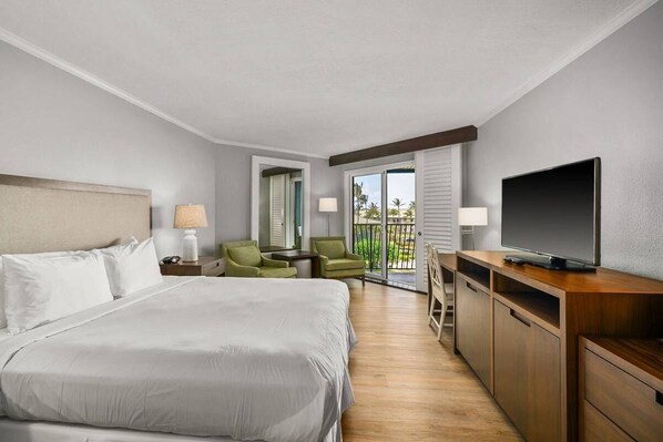 Habitación de hotel con una cama grande, televisión, escritorio y balcón con vistas a palmeras.