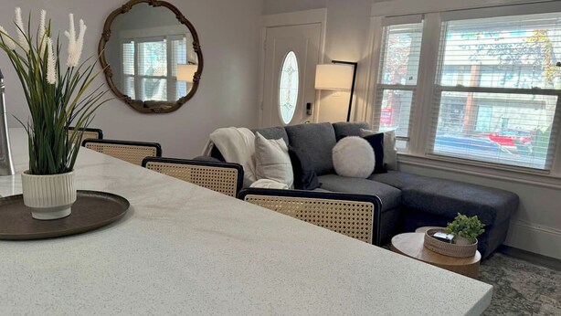 A living room with a dining table, a sofa, a chair, a mirror, and a window with a view of the street. - 2 BD/2 BA in Historic Downtown Sacramento -Beautiful Backyard, Centrally Located (Sacramento)