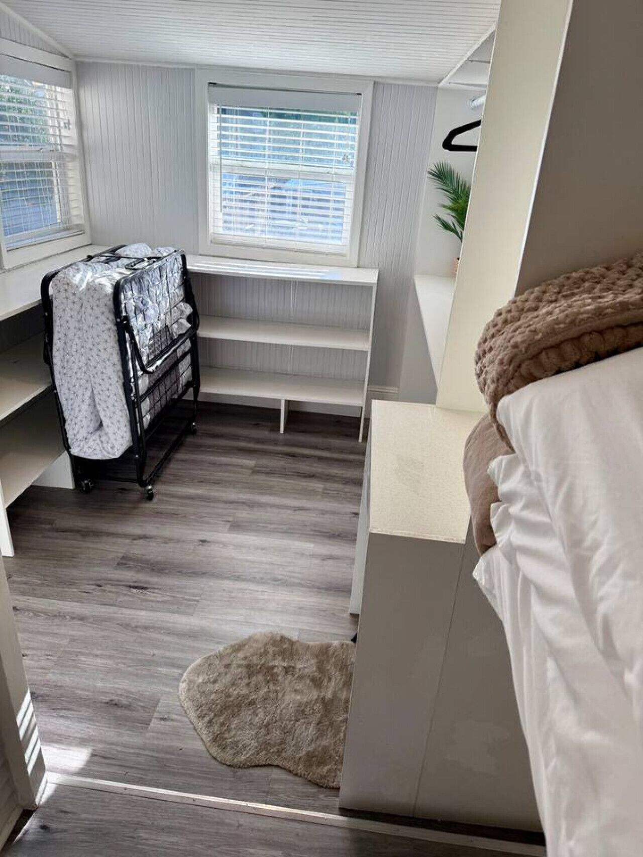Ett litet rum med en våningssäng, ett litet skrivbord, ett fönster med persienner och en förvaringsenhet.