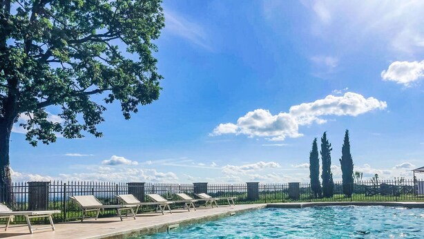 A swimming pool with clear blue water, surrounded by a tiled deck and lounge chairs.