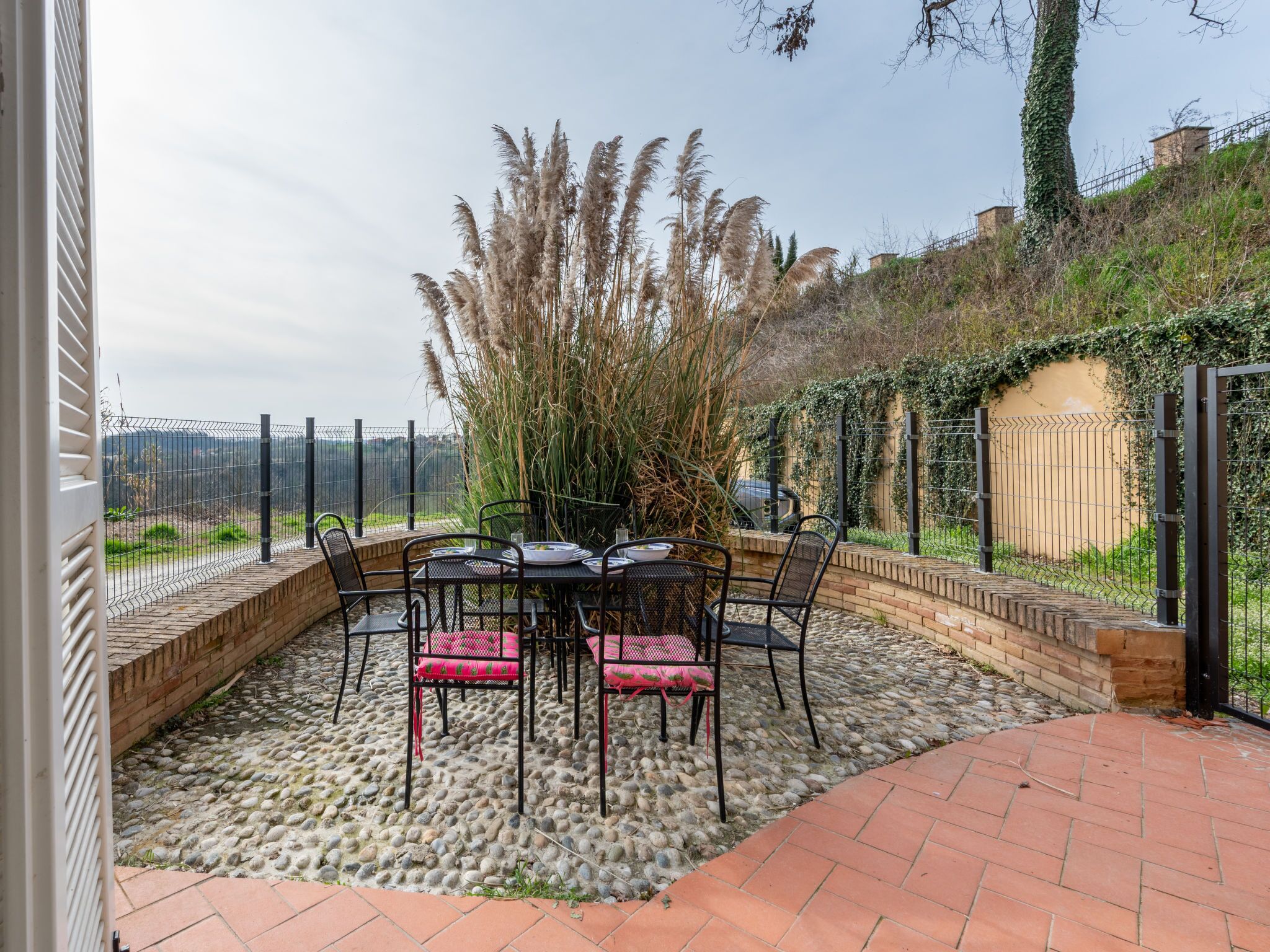 An outdoor patio with a table and chairs, surrounded by a stone wall and a fence.