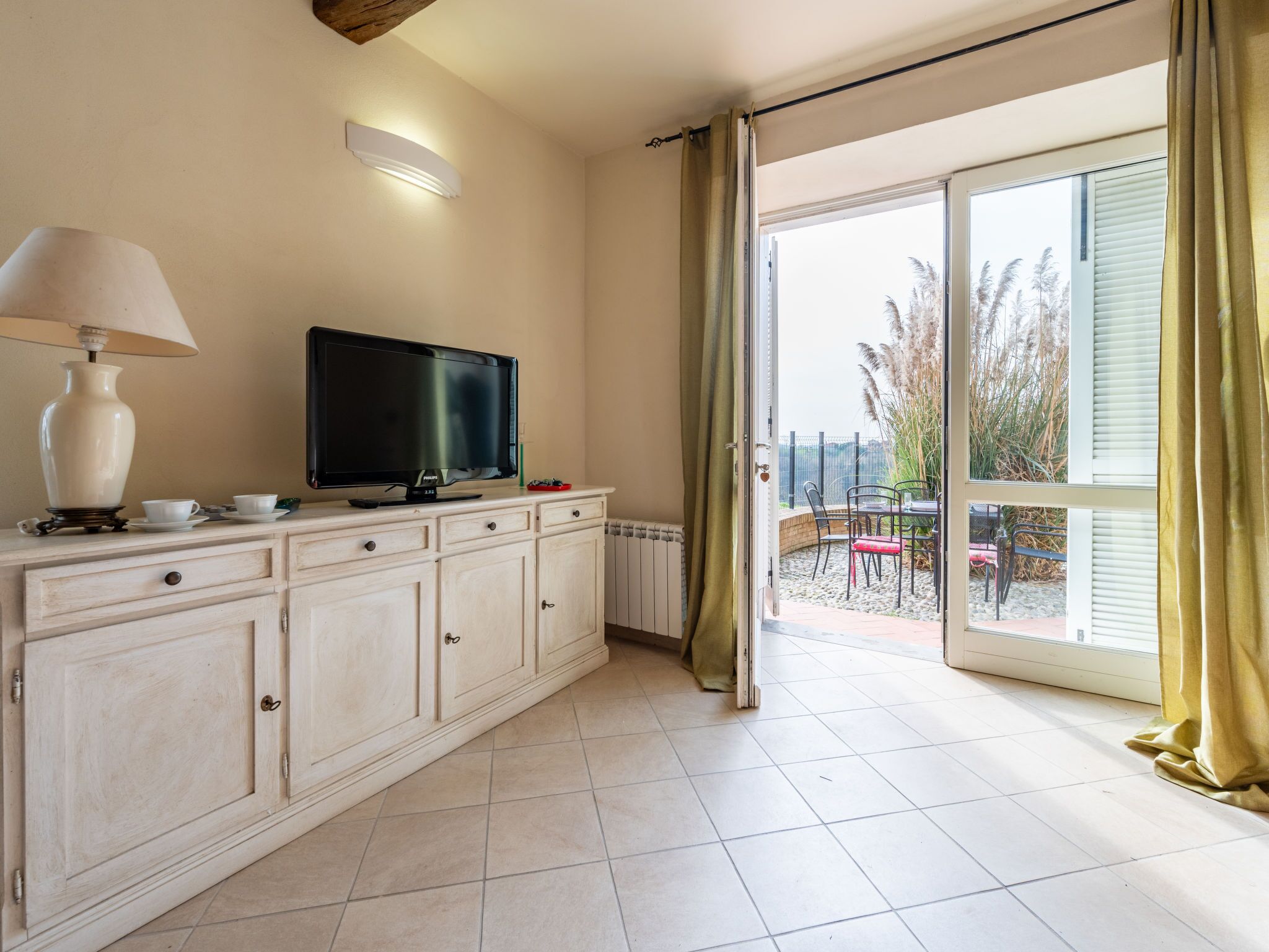 A room with a TV on a cabinet, a lamp, and a view of an outdoor patio.